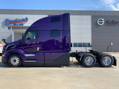 Volvo VNL64T860 sleeper cab semi-truck in purple finish, side view, 6x4 configuration parked in front of a Volvo dealership.