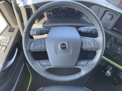 Volvo steering wheel and dashboard in a 2026 Volvo VNL64T860, showing steering wheel with Volvo emblem and control stalks, digital gauge cluster in the background.