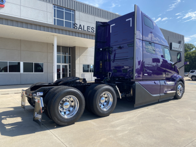 Volvo VNL64T860 truck cab and rear wheels in a dealership lot, purple sleeper cab with chrome wheels and triple-axle setup.