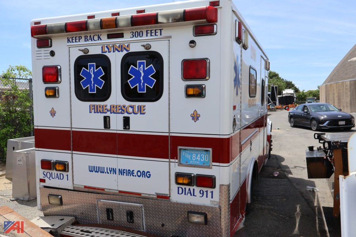 Ambulance rear view showing LYNN Fire/Rescue branding, Star of Life symbols, emergency lights, and rear doors with text; website URL and 911 dial text visible.