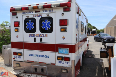 Ambulance rear view showing LYNN Fire/Rescue branding, Star of Life symbols, emergency lights, and rear doors with text; website URL and 911 dial text visible.