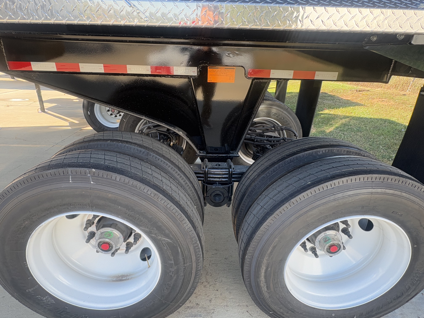 Dual rear axles with tires on a trailer chassis; label on suspension area and underside shows components but no legible text.