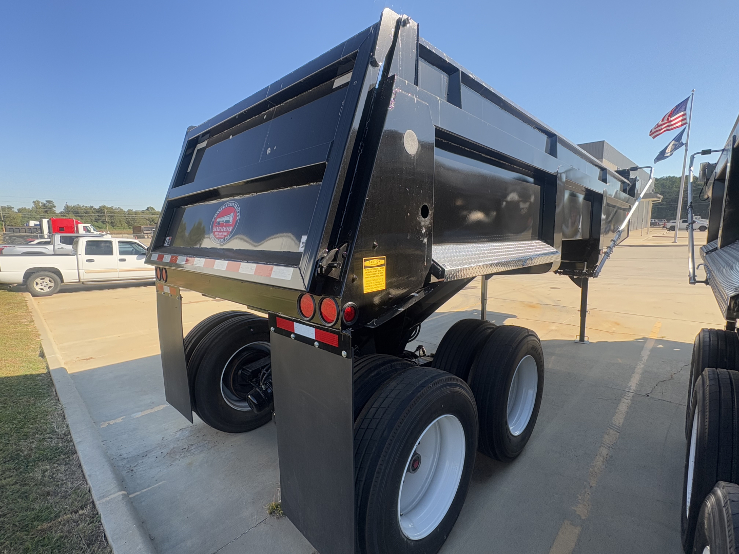 Dump trailer showing dual rear axles and dump bed with black paint and white wheels, side marker lights, and support legs visible.