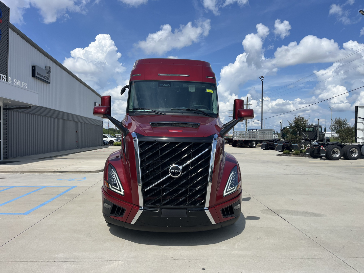 Front view of a red 2026 Volvo VNL64T840 tractor truck in a dealership lot, chrome grille with Volvo emblem, large windshield, and side mirrors.