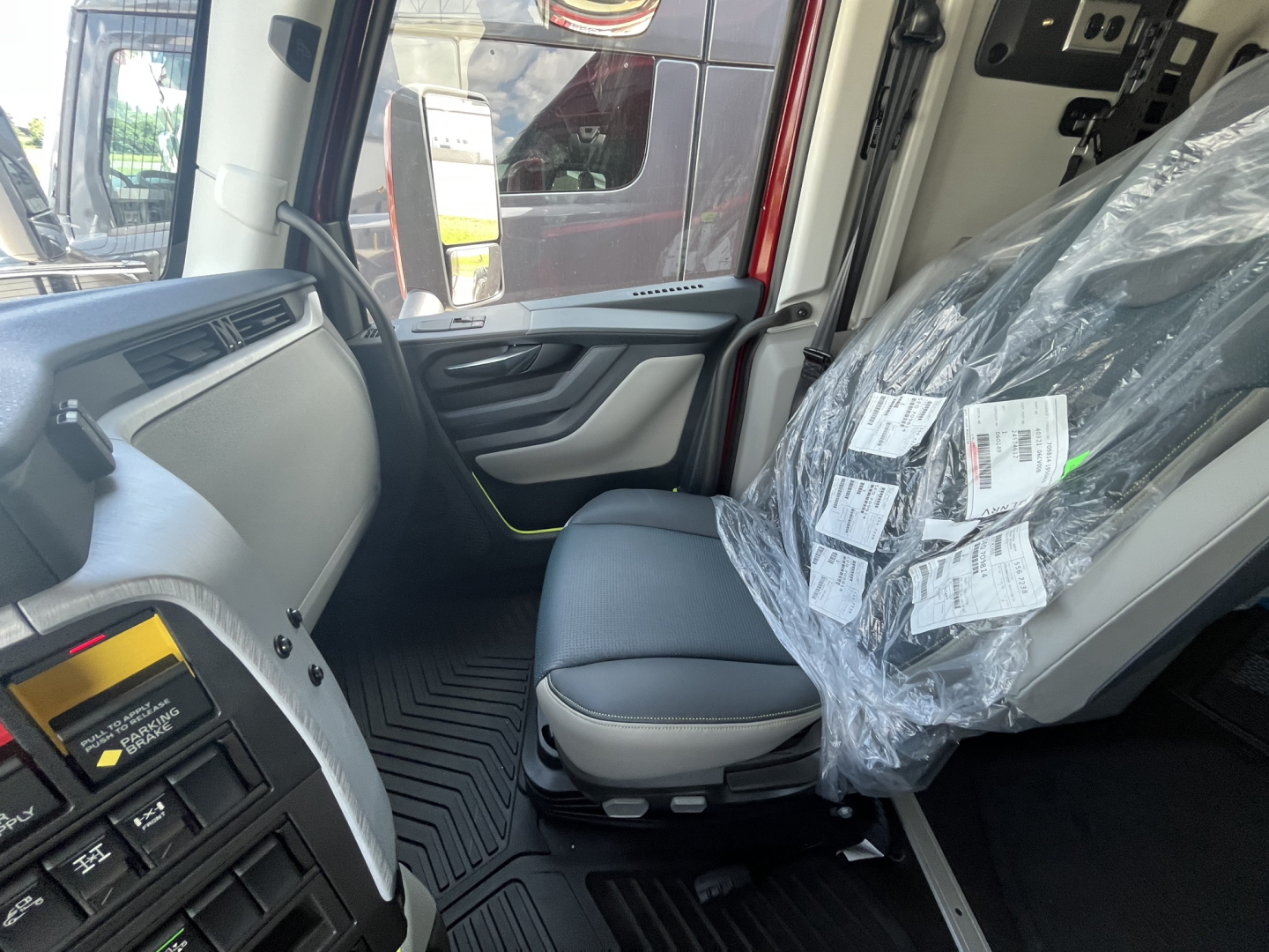 Truck cab interior with driver seat and plastic-wrapped passenger seat; dashboard with controls and door panel visible.