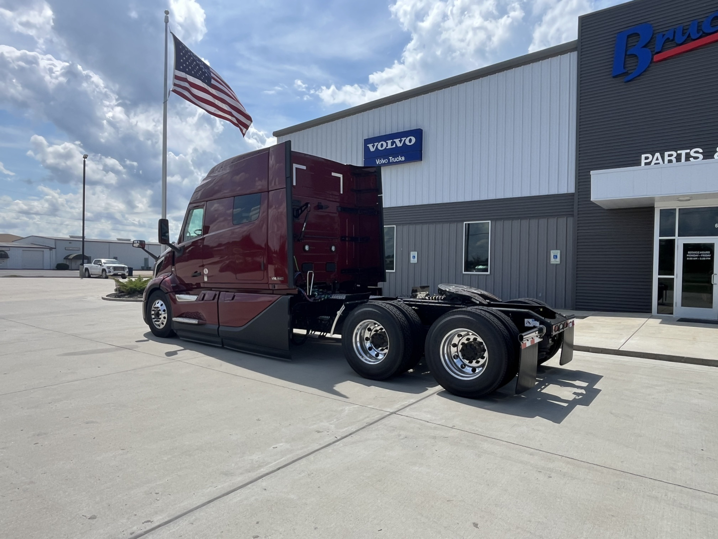 2026 Volvo VNL64T840 tractor side view showing the sleeper cab, chassis, rear dual wheels, and Volvo dealership building in background.