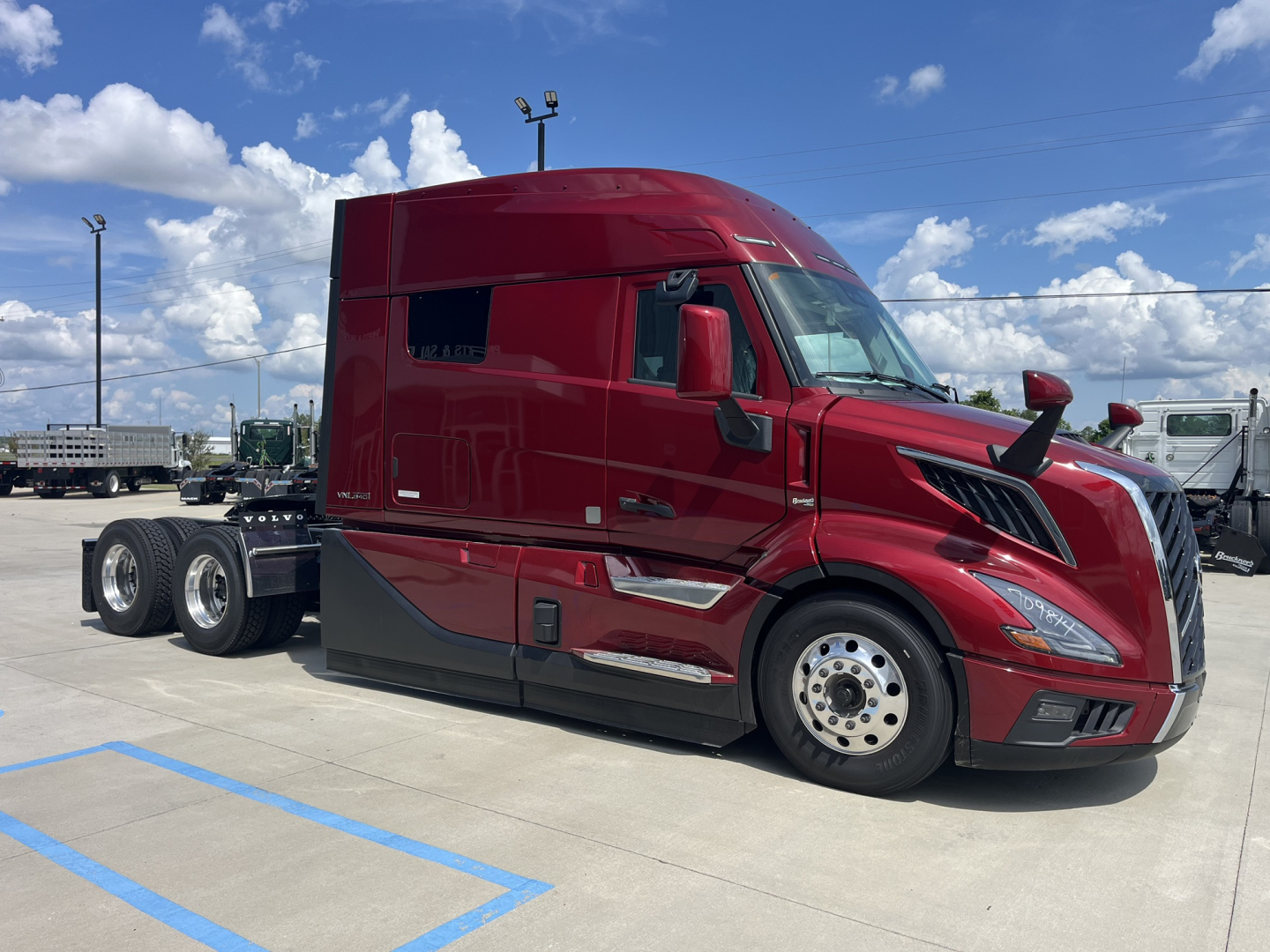 Red Volvo VNL64T840 truck cab in a dealership lot, side view. Visible text on the side windows and body panels, with details of the truck such as the large sleeper cab and chrome wheels.