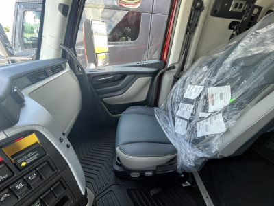 Truck cab interior with driver seat and plastic-wrapped passenger seat; dashboard with controls and door panel visible.