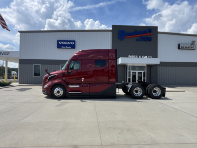Volvo VNL64T840 sleeper tractor in red side view showing stock truck dealership building and Bruckner’s logo.