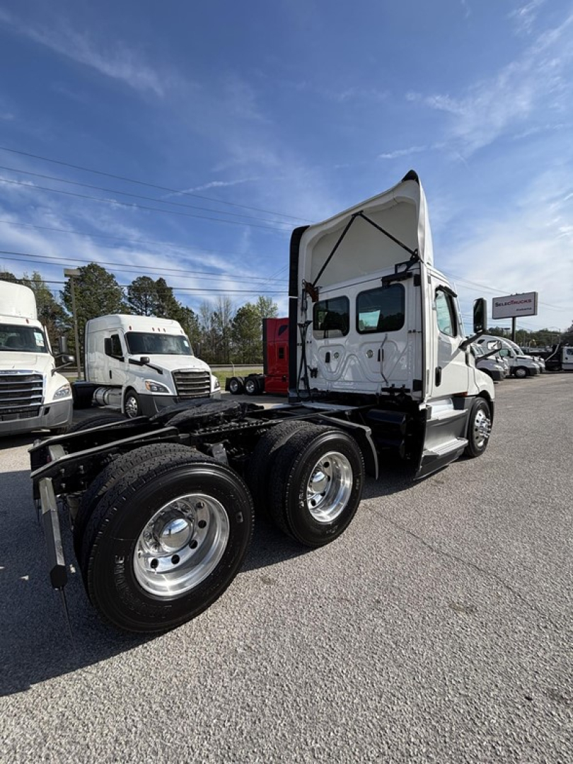 Freightliner Cascadia 126 day cab tractor with raised cab and dual rear axles, front cab side view, white exterior, chrome wheels, blue sky.