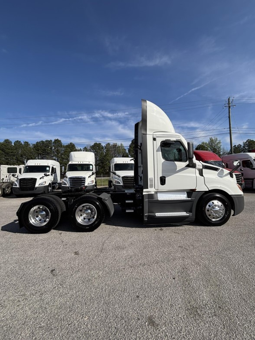 Truck side view of a white 2021 Freightliner Cascadia 126 day cab with three axles and tandem rear wheels.