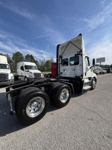 Freightliner Cascadia 126 day cab tractor with raised cab and dual rear axles, front cab side view, white exterior, chrome wheels, blue sky.