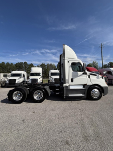Truck side view of a white 2021 Freightliner Cascadia 126 day cab with three axles and tandem rear wheels.