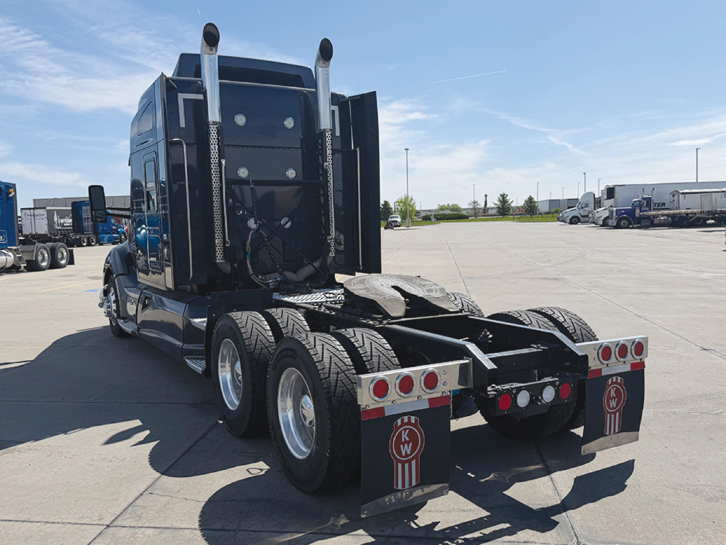 Kenworth T680 tractor rear view showing dual rear axles and fifth wheel with mud flaps and tail lights.