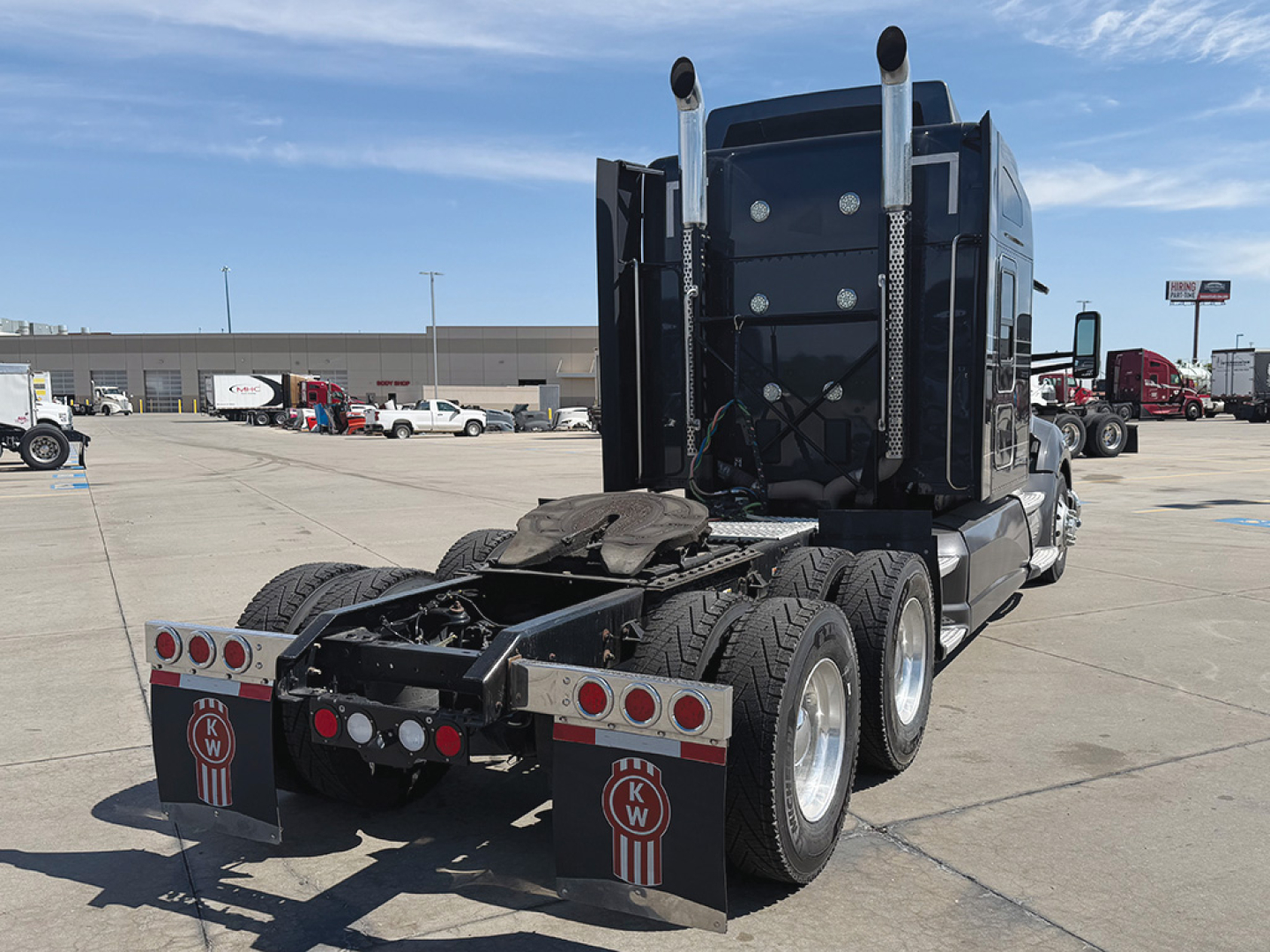 Kenworth T680 tractor rear view showing fifth wheel and dual rear axles with mud flaps and branding.
