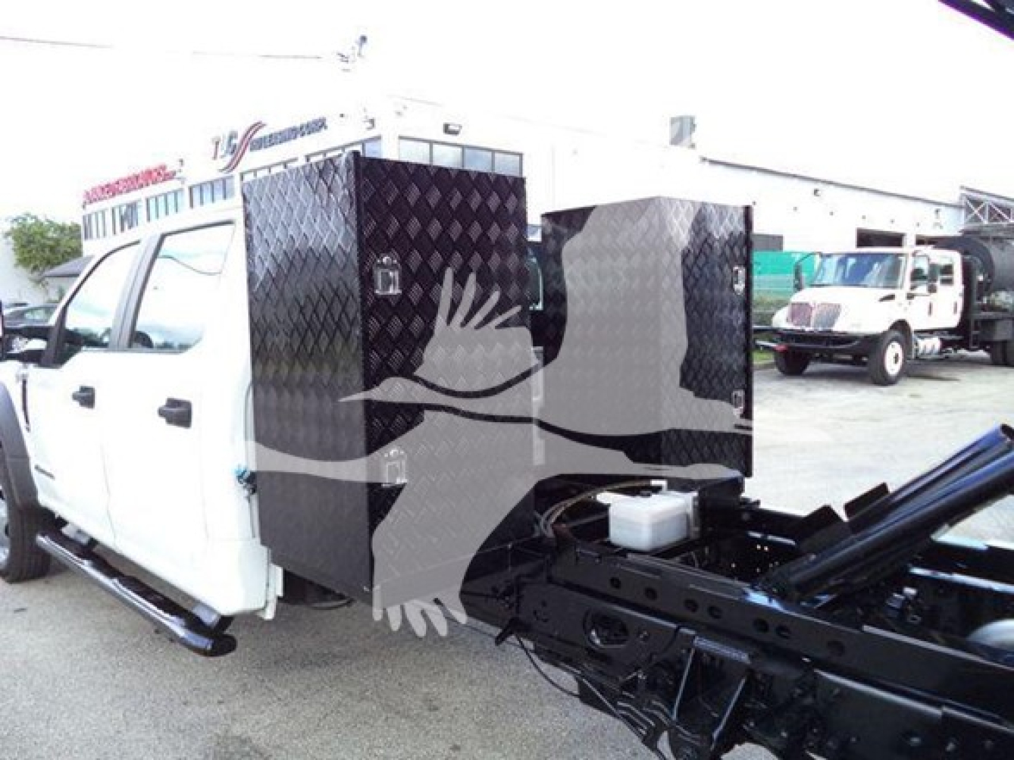 Ford F-550 dump truck cab rear with diamond plate tool boxes and hydraulic chassis components visible.