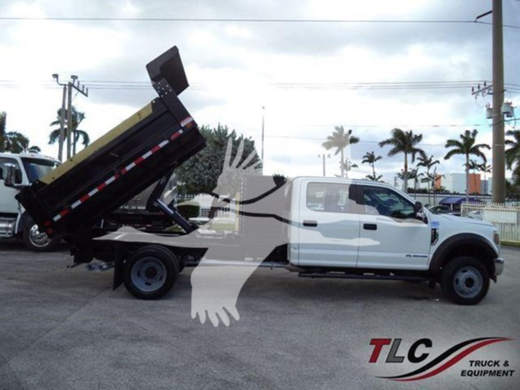 Ford F-550 dump truck with hydraulic dump bed raised, white cab, black dump body in a dealership lot.