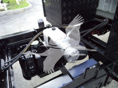Ford F-550 chassis area showing hydraulic pump/valve assembly and wiring harness in engine bay.