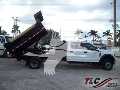 Ford F-550 dump truck with hydraulic dump bed raised, white cab, black dump body in a dealership lot.