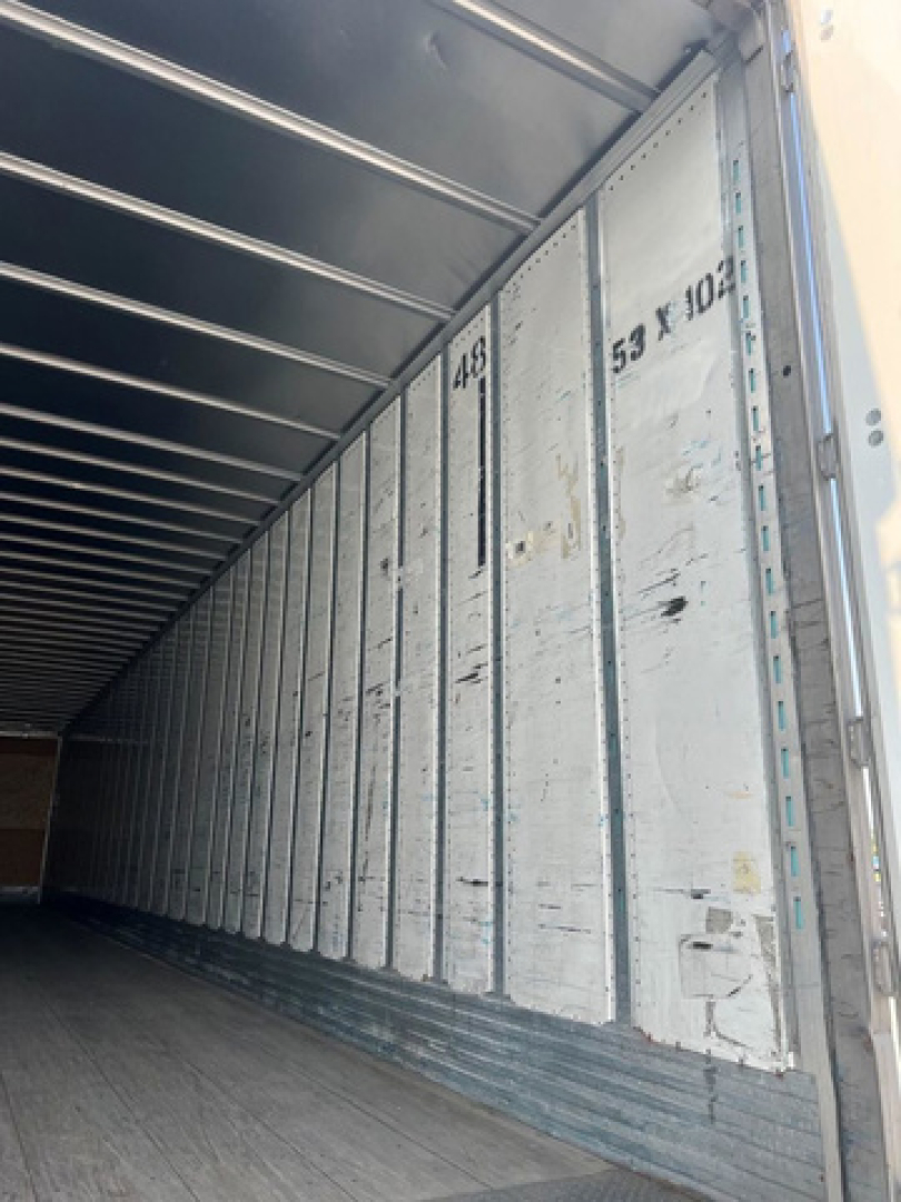 Inside view of a trailer cargo area with metal walls and overhead support beams; stamped numbers on the side panels; light from the open doorway.