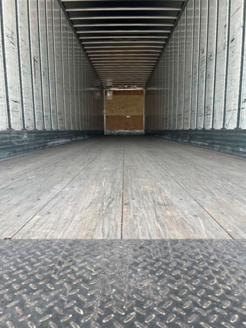 Trailer interior showing empty cargo space with wooden floor and metal sidewalls; front wall with wooden bulkhead in distance.