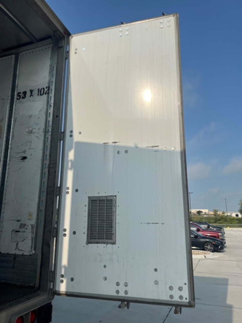 Van trailer side with ventilated access panel and riveted aluminum skin; open rear door reveals interior steel frame and numbers along edge.