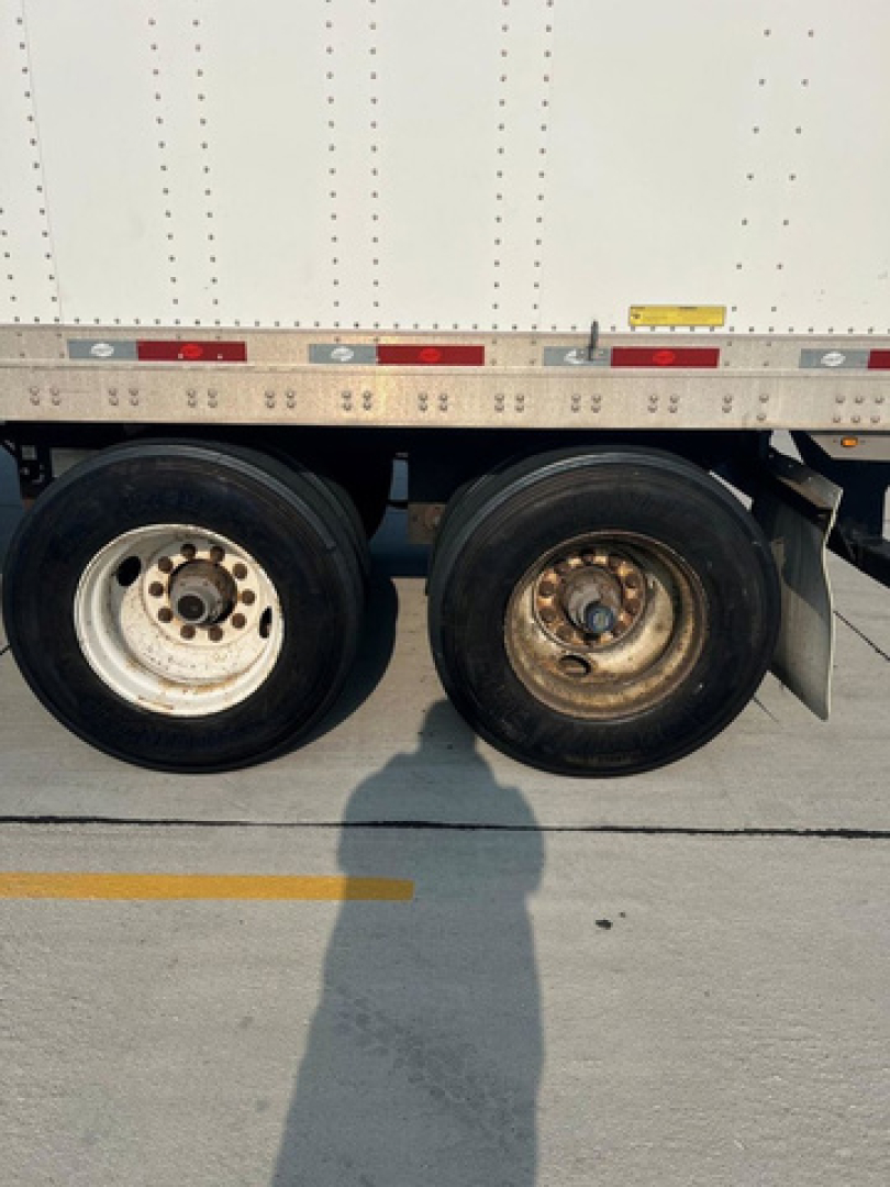 Dual rear wheels of a utility trailer with white body; no legible brand text or model numbers visible on the image.