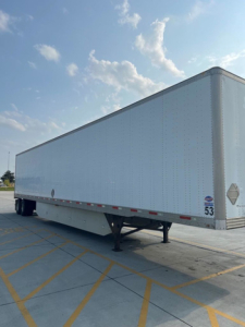 Side view of a white rectangular trailer with a gooseneck hitch visible at the front, located in a parking lot with yellow lines.