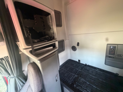 Volvo VNL64T760 sleeper cab interior showing overhead storage compartment with open panel, window, and control panel on right; floor mat visible.