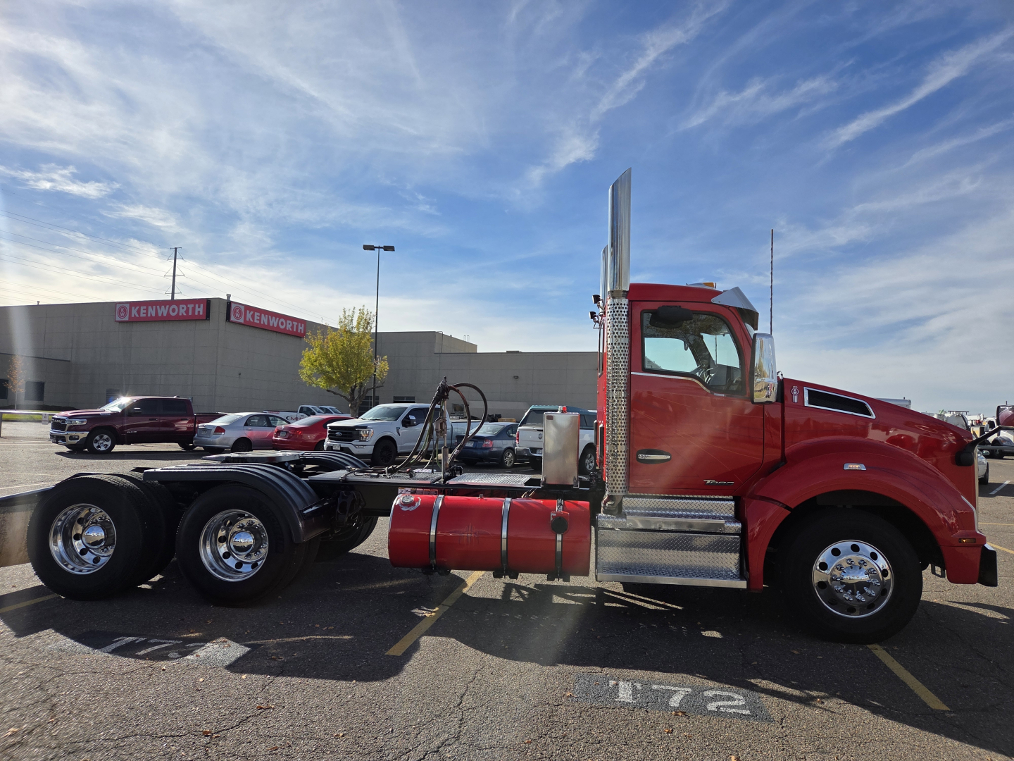 Kenworth T880 2020 conventional daycab truck side view showing red cab, chrome fuel tanks, tall exhaust stacks, and dual rear axles with empty trailer frame.