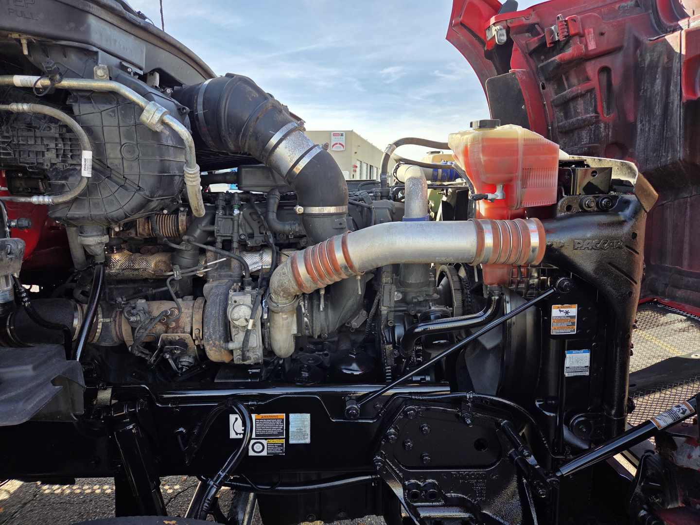 Kenworth T880 engine bay showing intake hoses and coolant reservoir in cab-forward area.