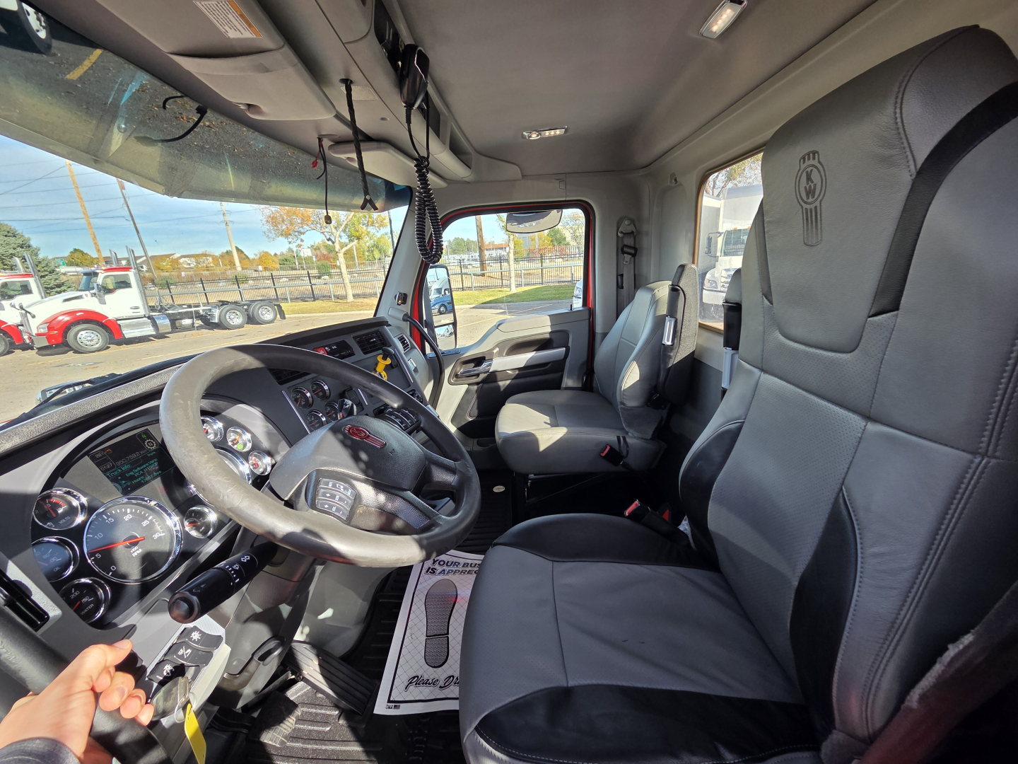 Kenworth T880 truck interior showing steering wheel, dashboard gauges, driver seat, and passenger seat in a daycab with gray upholstery.