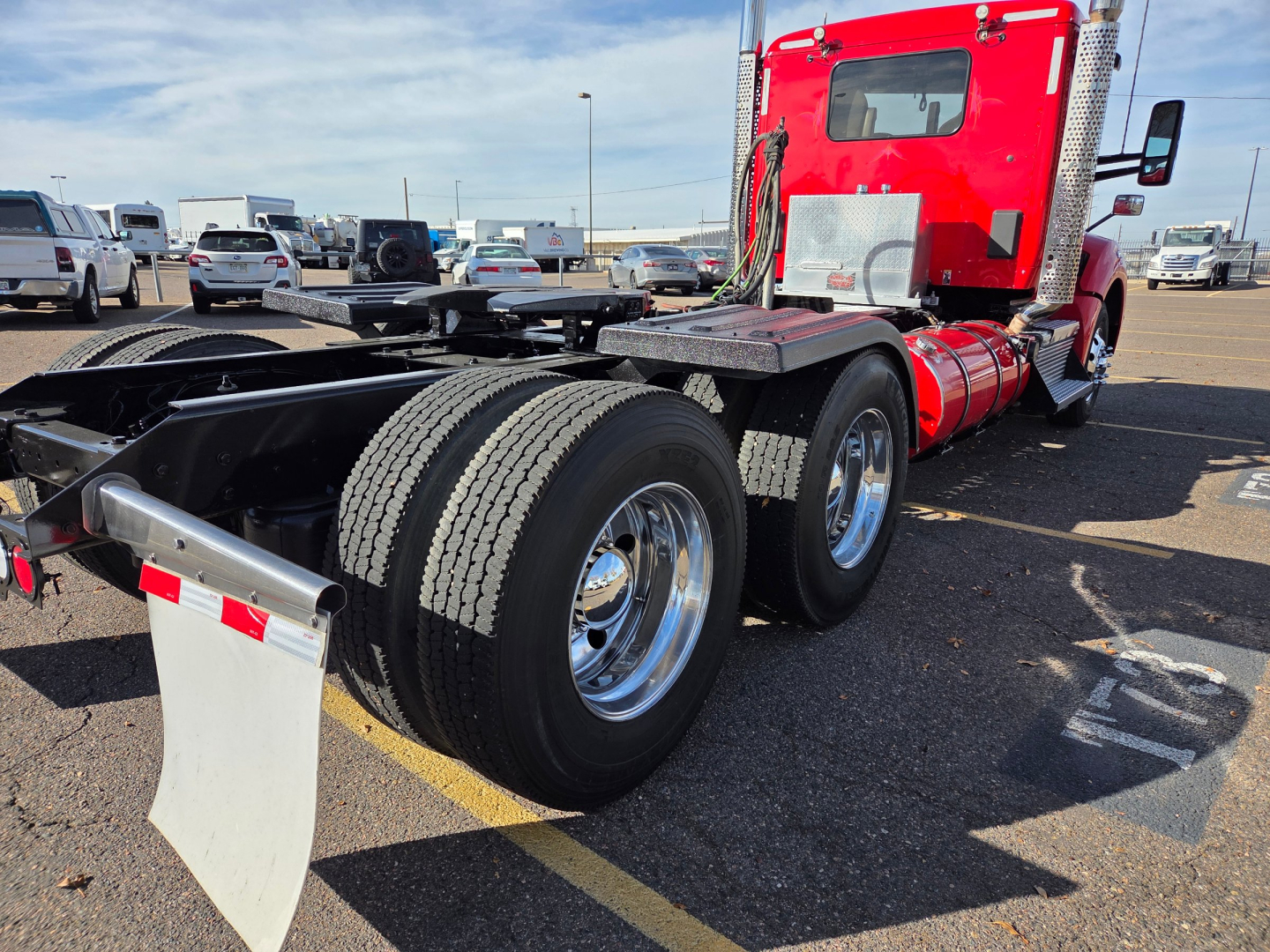 Kenworth T880 tractor rear view showing dual rear axles and chrome wheels with red cab in background; fifth wheel, fuel tanks, and chassis visible.
