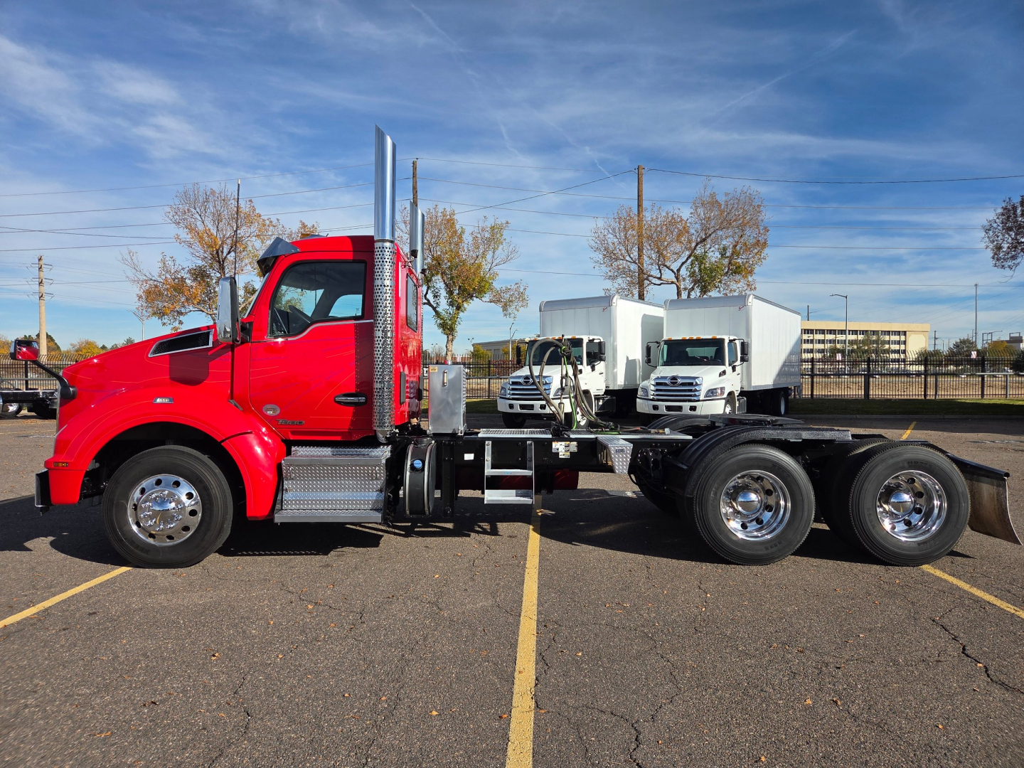 Kenworth T880 conventional daycab truck side view showing red cab and white dump trailers in background.