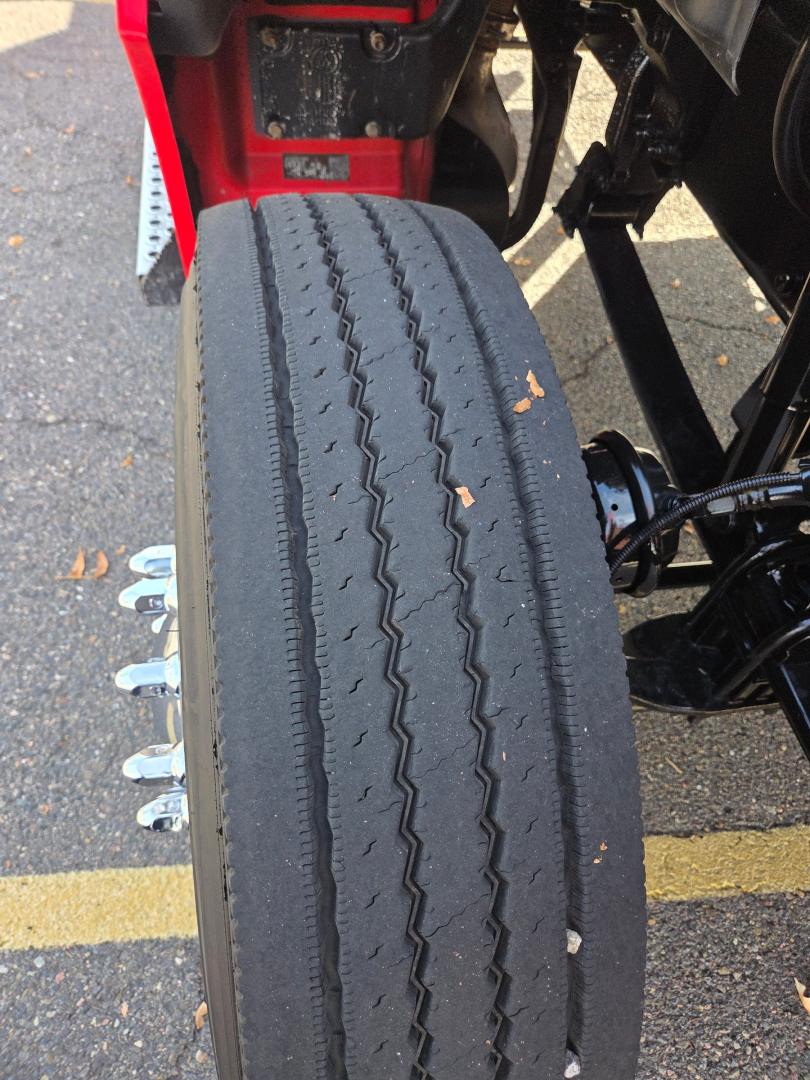 Kenworth T880 wheel and suspension area showing dual rear wheel hub and tire tread with orange leaf debris. Partial undercarriage and frame visible.