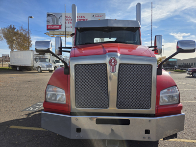 Kenworth T880 front view showing large chrome grille, red cab, bumper, and side mirrors.