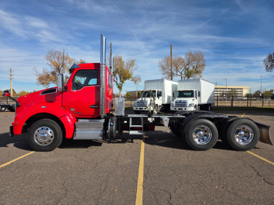 Kenworth T880 conventional daycab truck side view showing red cab and white dump trailers in background.