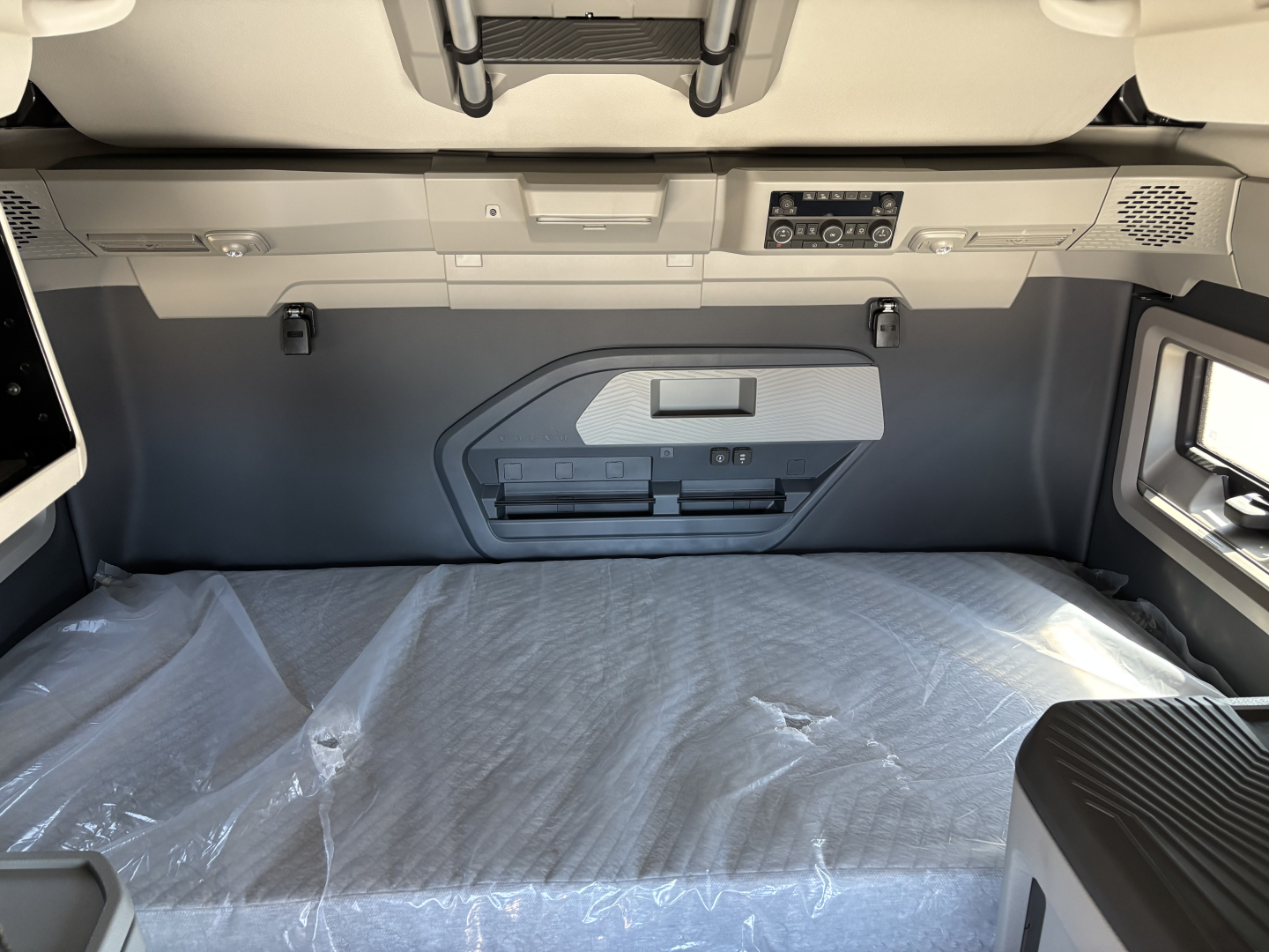 Truck cab interior cargo area of a 2026 Volvo VNL showing storage panel and sleeper bed with plastic cover.