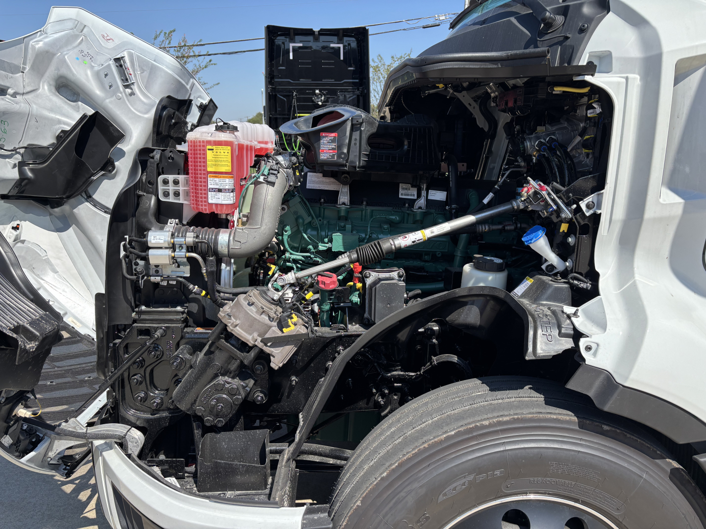 Volvo VNL64T860 truck engine bay view showing green engine, hoses, and exposed components with front wheel visible.