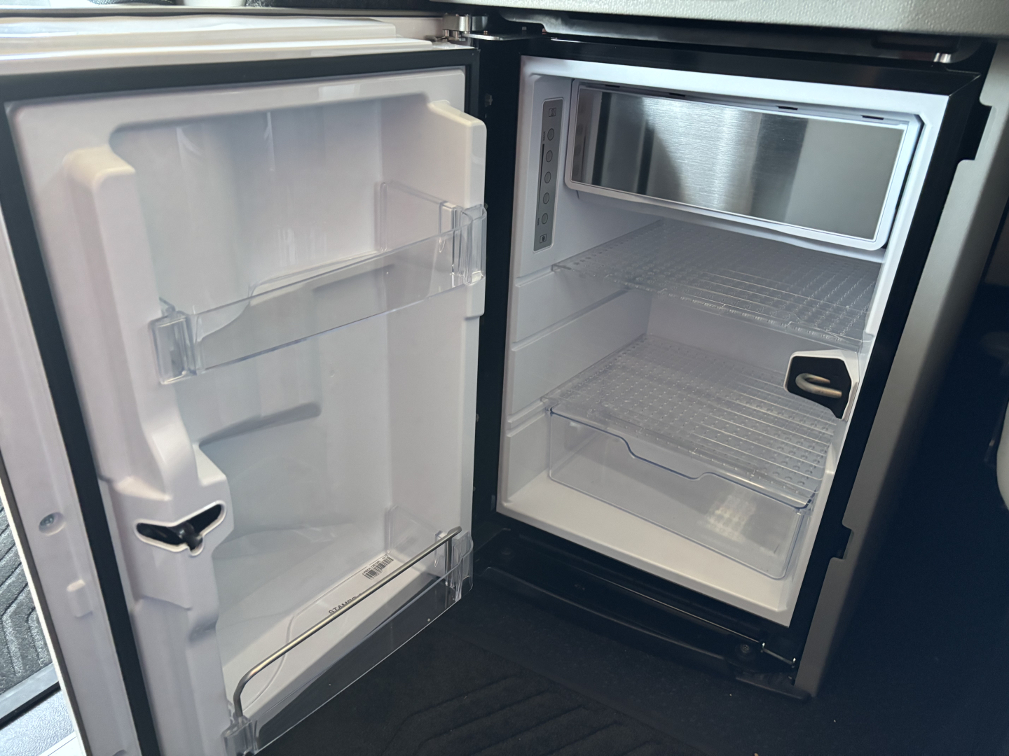 Refrigerator and freezer compartments inside a new Volvo VNL64T860 truck, open doors showing empty shelves and interior light.