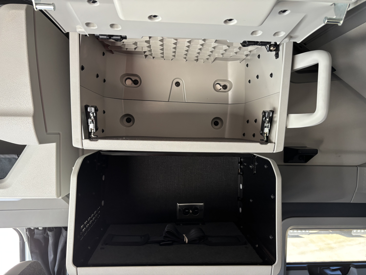 Volvo VNL64T860 cab interior showing open overhead storage compartment and lower storage bay with wiring and mounting brackets.