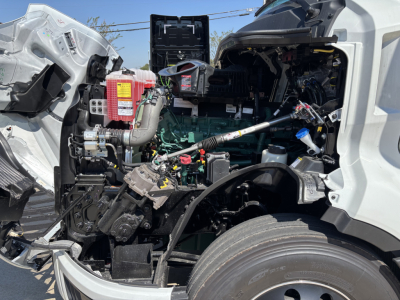 Volvo VNL64T860 truck engine bay view showing green engine, hoses, and exposed components with front wheel visible.