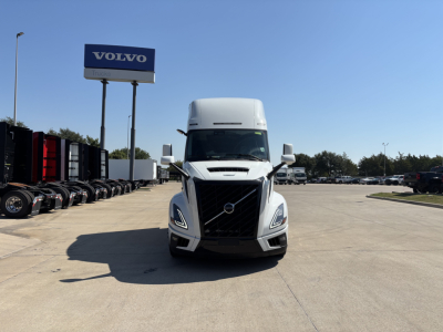 Front view of a white Volvo VNL64T860 truck in a dealership lot with a Volvo sign in the background.