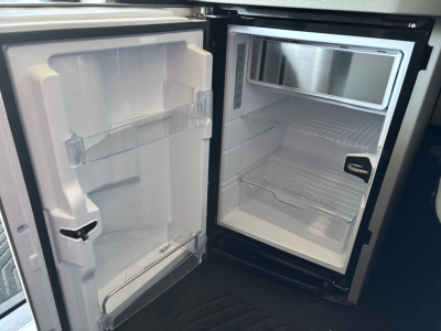 Refrigerator and freezer compartments inside a new Volvo VNL64T860 truck, open doors showing empty shelves and interior light.