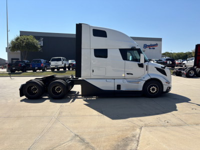 Truck side view showing a white Volvo VNL64T860 conventional sleeper semi-truck with three axles and a high sleeper cab.