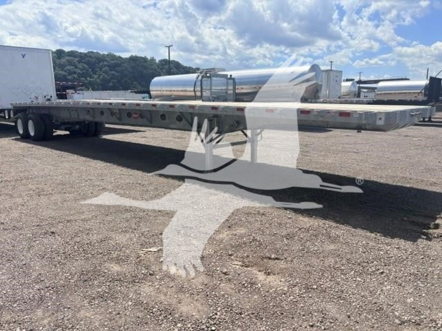 Trailer flatbed showing long steel deck with tandem axles and a cylindrical aluminum tank mounted on the chassis.