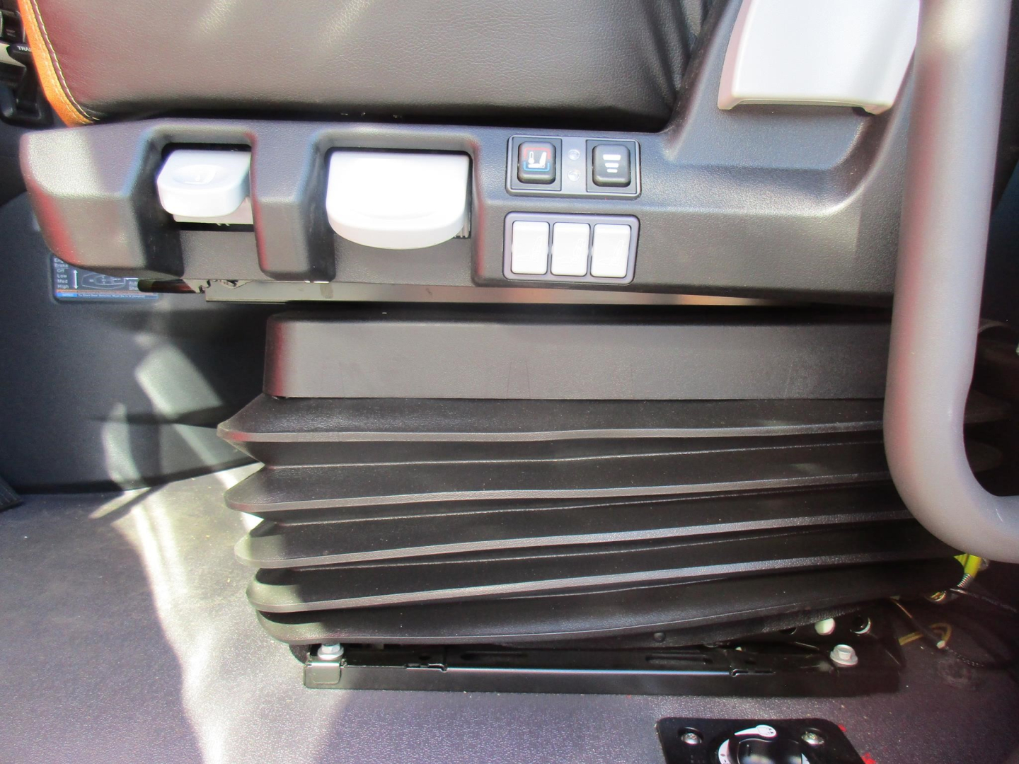 Front cab area of a new Western Star 47X showing seat controls and a ribbed black component (likely HVAC or support) under the dash.
