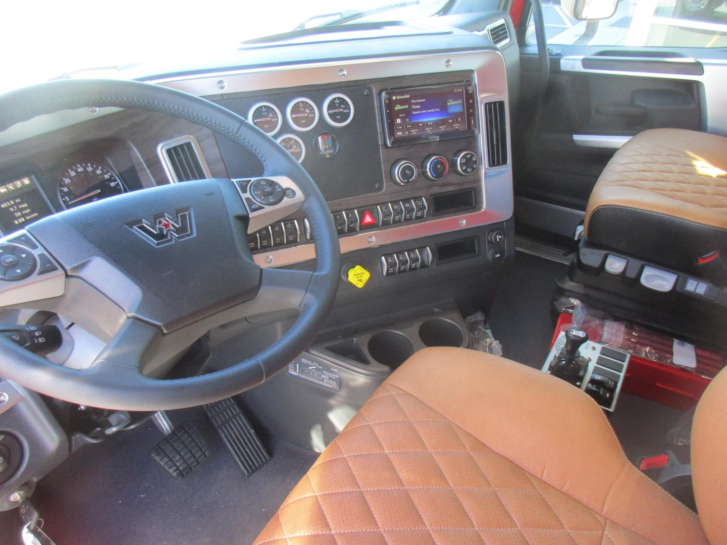 Truck cab interior showing steering wheel, dashboard with gauges, center console, and tan quilted seat.