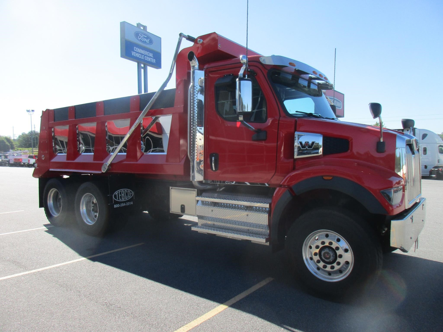 Western Star 47X dump truck in red, side view with dump bed, front grille, dual rear wheels, chrome steps, and black exhaust stacks.