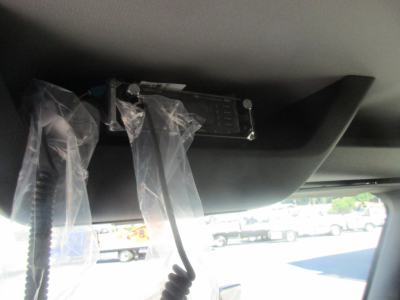 Cab interior showing a mounted device with plastic protective covers and wiring harnesses; visible hardware includes a rectangular badge with screws and a black surface.